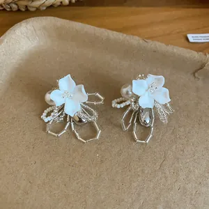Close-up detail of elegant white shell flower earrings with pearls and clear beads.