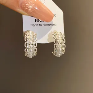 Primer plano de elegantes pendientes en C con perlas, pedrería y detalles de encaje