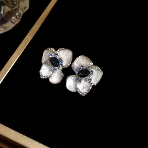 Dettaglio di eleganti orecchini a lobo a fiore in smalto bianco e cristalli blu