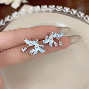 Vista macro detallada de pendientes florales de esmalte azul con circonitas y perlas