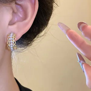 Primer plano de pendientes dorados en forma de C con perlas y pedrería en borde festoneado.