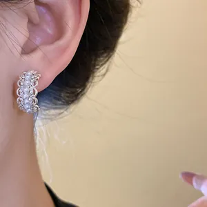 Detalle de pendientes de botón en C de plata con perlas y cristales usados en la oreja