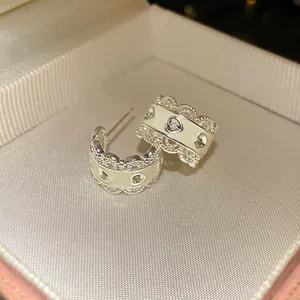 Primer plano de pendientes de aro en C plateados con borde de encaje y delicados corazones