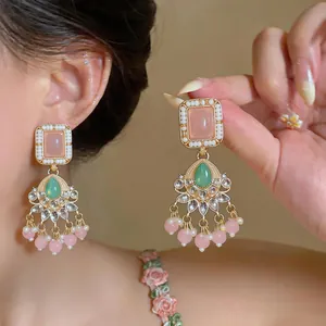Detail of retro luxury tassel earrings with pink resin and rhinestones on model and hand.