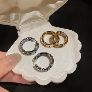 Close-up detail of 18K gold plated zircon hoop earrings displayed in a white shell box