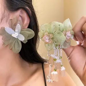Elegantes pendientes de flores de gasa verde oliva con borlas de perlas en mano