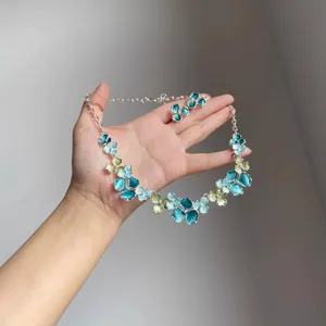 Hand holding floral necklace and earrings set in blue and green enamel tones
