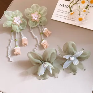 Detalle de elegantes pendientes de flores de gasa con perlas y borlas de cuentas