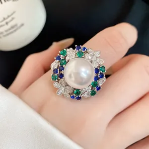 Close-up of a vintage pearl ring with blue and green zirconia stones on a hand.