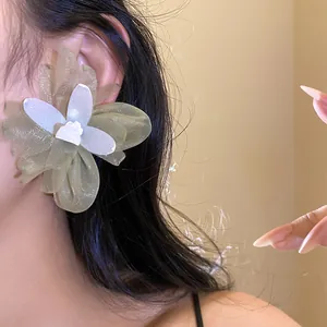 Primer plano de elegantes pendientes grandes de flor de gasa usados en la oreja del modelo.