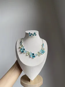 Elegant blue and green enamel flower necklace and earrings set on a white display