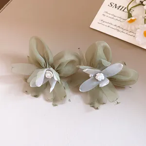 Primer plano de elegantes pendientes de flor de gasa verde salvia con centros de perlas