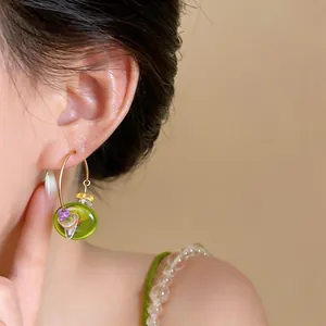 Close-up view of a green resin stone beaded hoop earring worn on a model's ear