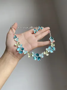 Hand holding an elegant flower necklace and earrings set with blue and green enamel petals