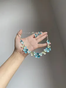 Handheld view of elegant floral necklace and earrings set in blue and green enamel