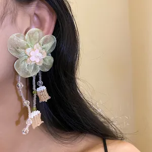 Detalle de pendientes de flor de gasa verde claro con perlas y borlas de cuentas.