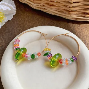 Close-up of gold hoop earrings with colorful resin beads on a white ceramic plate