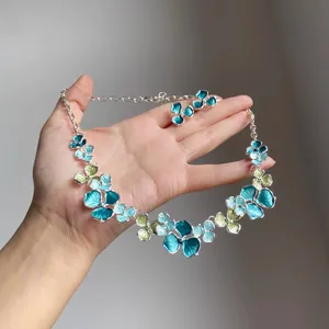 Detailed view of teal blue enamel flower necklace and earrings set held in hand