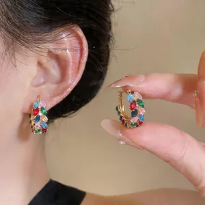 Detailed close-up of vibrant colorful zircon wheat-shaped gold hoop earrings worn on ear.
