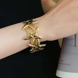 Detailed macro view of a gold-finish metal starfish open bracelet worn on a female wrist