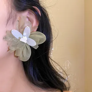 Primer plano detallado de un gran pendiente de flor de gasa verde oliva en modelo joven