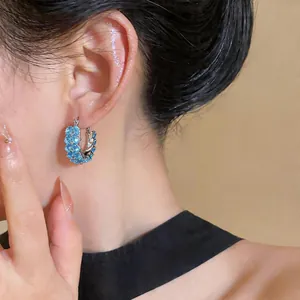 Close-up of vibrant blue zircon hoop earrings on model, light luxury style.