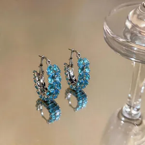 Close-up of blue zircon wheat ear hoop earrings on a reflective surface