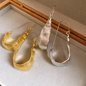 Macro view of luxury minimalist gold and silver textured U-shaped designer drop earrings
