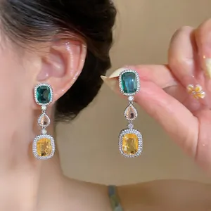 Close-up of vintage drop earrings with colorful square and teardrop zircons on model.