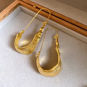 Detail view of gold U-shaped earrings with unique hammered texture in a wooden box