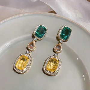 Close-up of vintage dangle earrings with green and yellow square zircons on a plate