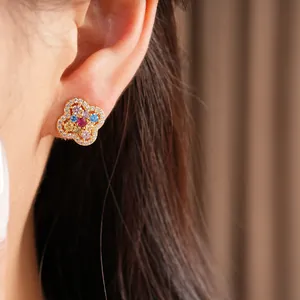 Detailed close-up of a colorful 14k gold plated flower stud earring worn on a person's ear