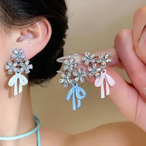 Detalle de elegantes pendientes florales con pedrería brillante y lazos de esmalte de colores