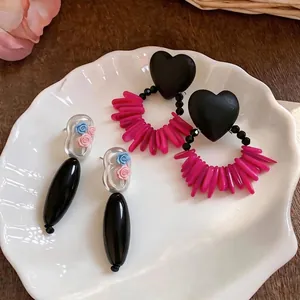 Handmade acrylic heart and floral drop earrings displayed on a white shell plate