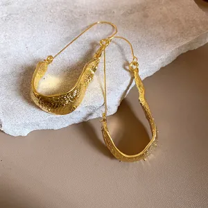 Detailed view of textured gold U-shaped earrings on a natural stone background