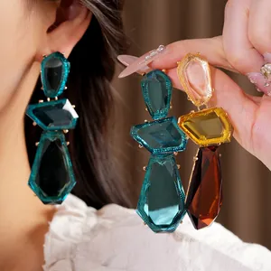 Close-up detail of oversized irregular geometric resin earrings in teal and amber.