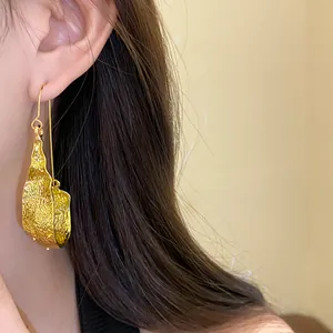 Detailed close-up showing the unique hammered texture of a gold U-shaped drop earring on ear
