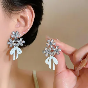 Detalle exquisito de pendientes de plata con flores de diamantes y lazos blancos suaves.