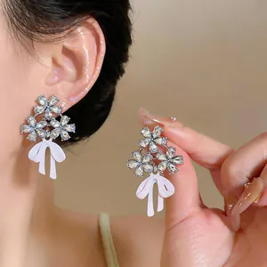 Detalle de elegantes pendientes de flor con diamantes y lazo blanco