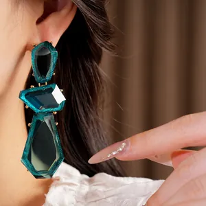 Macro detail view of large irregular dark green resin drop earrings worn by a model