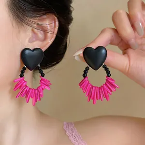 Detail view of stylish black heart earrings with vibrant pink acrylic fringe on model's ear.