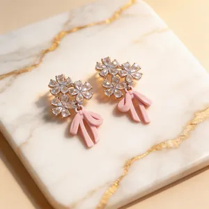 Primer plano de pendientes de flores con cristales y colgantes de lazo rosa esmaltado