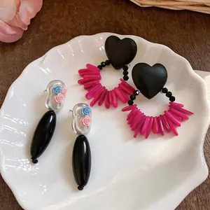 Macro detail of elegant handmade earrings with black heart, pink beads and floral accents