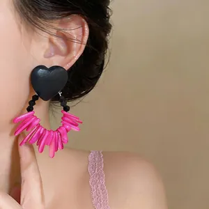 Close-up detail of black heart acrylic earrings with vibrant pink beaded tassels