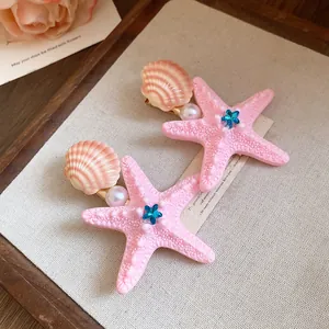 Close-up of pink starfish and shell hair clips with pearl and blue gem detail.