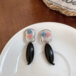 Close-up of acrylic floral drop earrings with black oval pendants on white plate