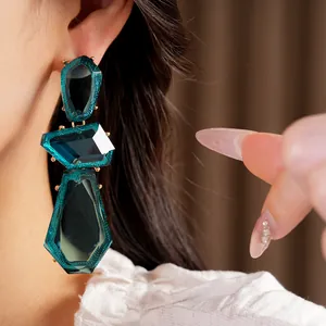 Close-up detail of oversized irregular teal resin earrings with gold trim on model