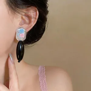 Close-up of elegant acrylic teardrop earrings with pink and blue rose details on model