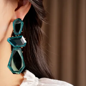 Detailed view of oversized irregular dark teal resin earrings with gold metallic claws.