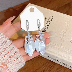 Close-up view of elegant silver earrings featuring white shell pendants and zircon stars.